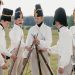 A group of historical reenactors in military uniforms stacking rifles outdoors in a field.